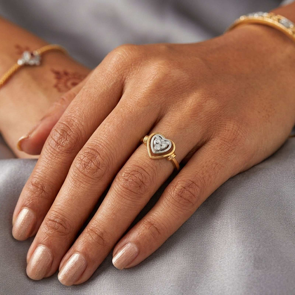 A close-up of a hand wearing a gold heart-shaped ring on a gray fabric background.