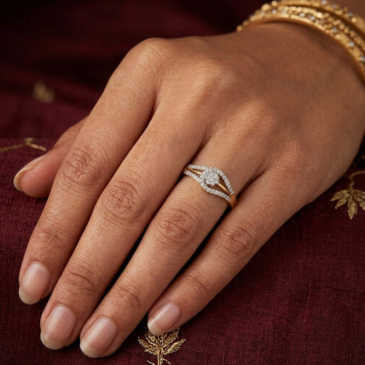 A close-up of a hand wearing a diamond ring with a gold and diamond band, resting on a deep maroon embroidered fabric background.