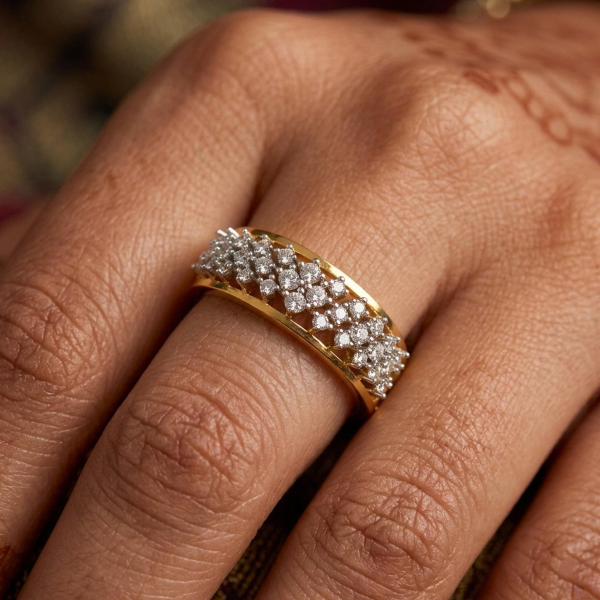 A close-up of a gold band ring set with multiple rows of sparkling clear stones, worn on a person's finger.