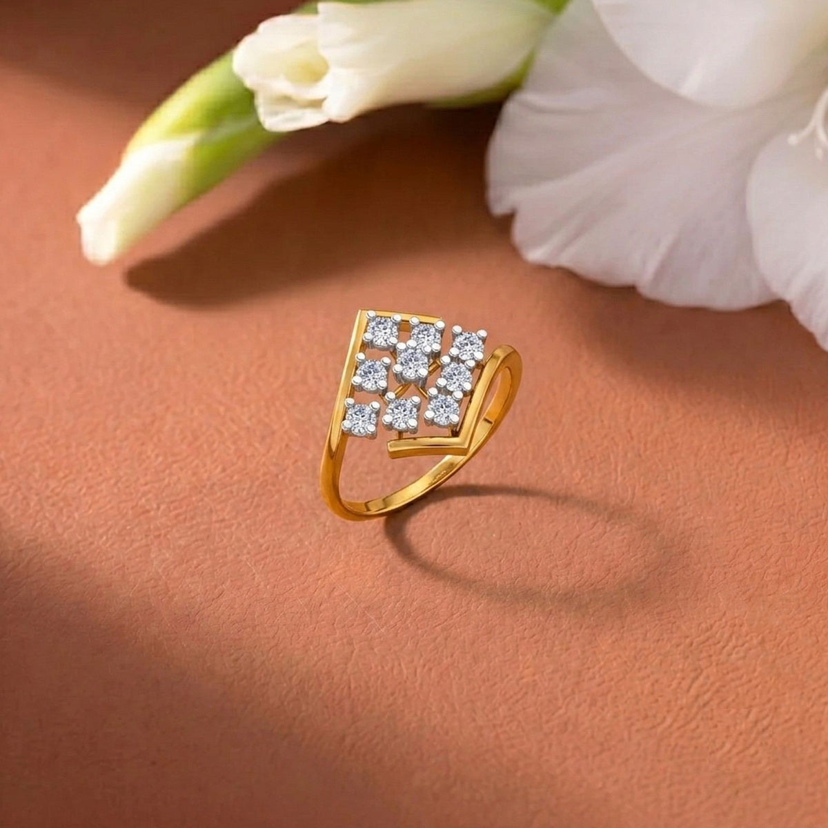 A gold ring with a square cluster, styled on a textured terracotta surface with soft white flowers in the background.