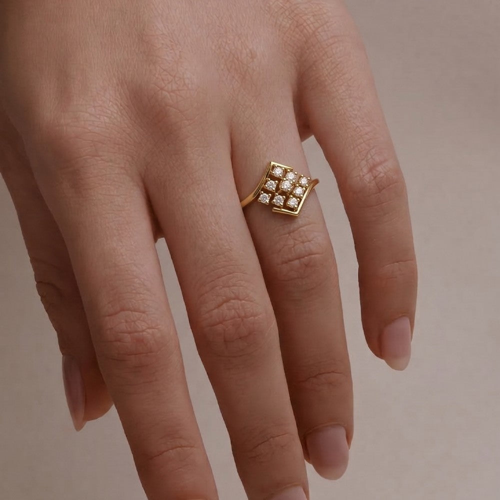 A gold ring with a square pavé setting, shown worn on a person's finger against a soft beige background.