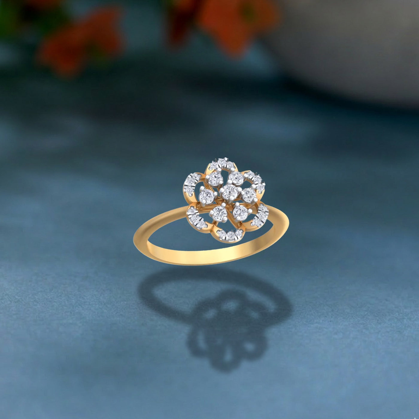 A gold ring with a floral design setting set, resting on a textured blue surface.