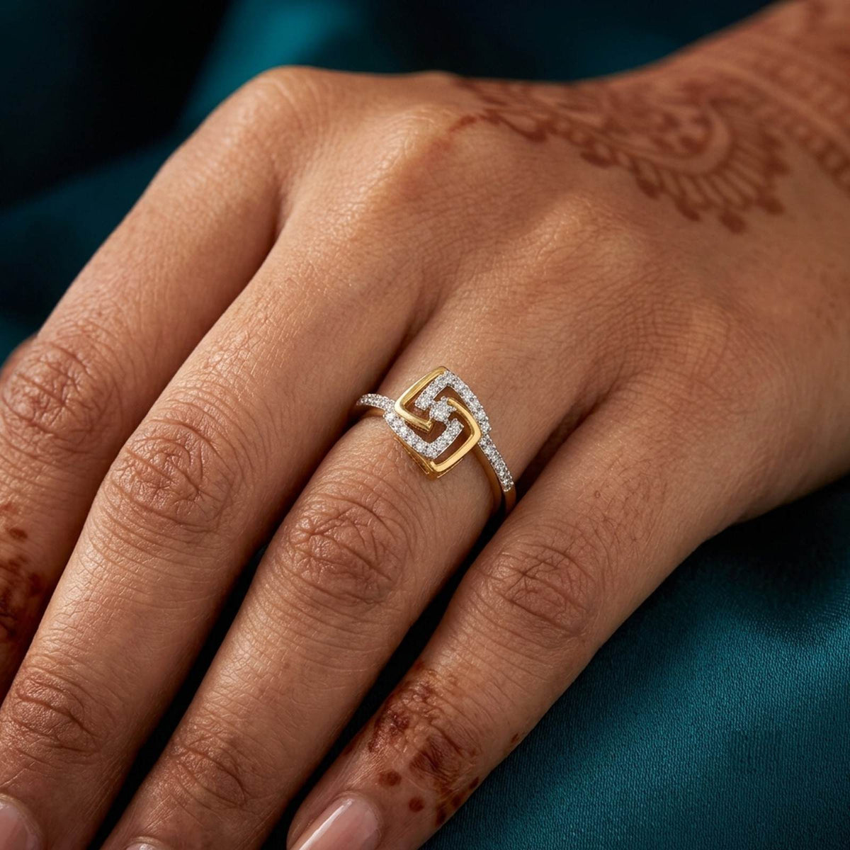 A close-up of a hand wearing a gold ring featuring a geometric square design set with small clear stones.
