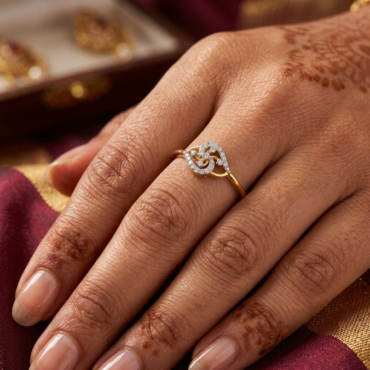A close-up of a hand wearing a gold and diamond ring on a background is a maroon.
