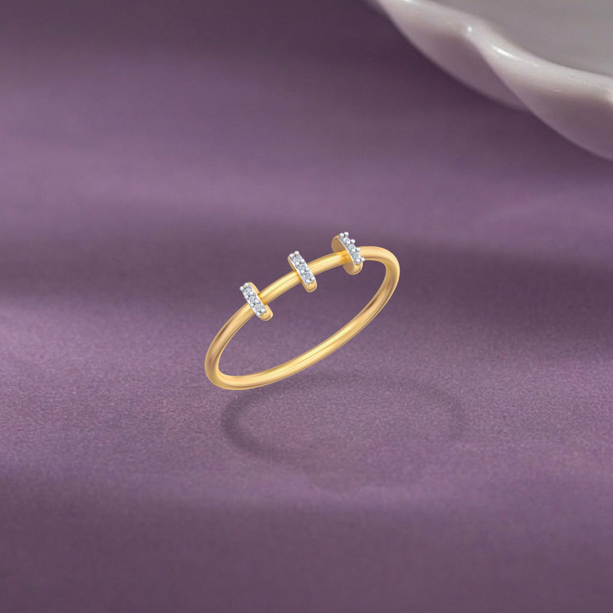 A delicate gold ring with three small horizontal bars, displayed on a textured purple surface.