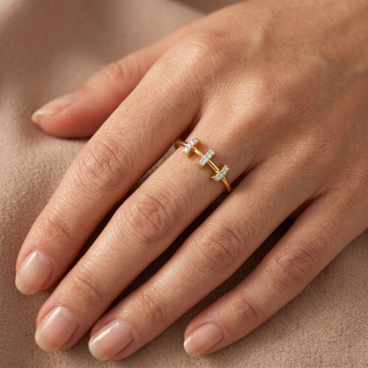 Gold ring with small diamonds on a hand against a beige background