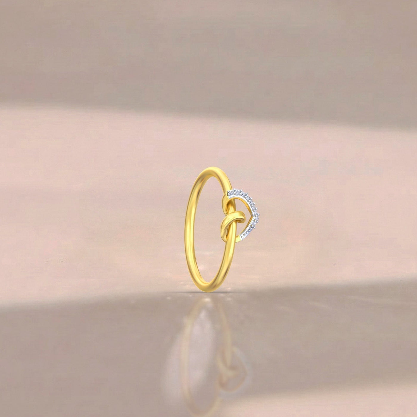 A delicate gold ring with a knot design, standing upright on a reflective beige surface.
