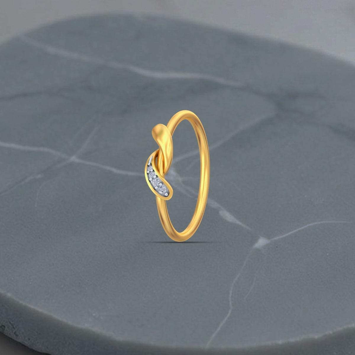 A gold ring with a twisted leaf design, displayed on a gray stone surface.