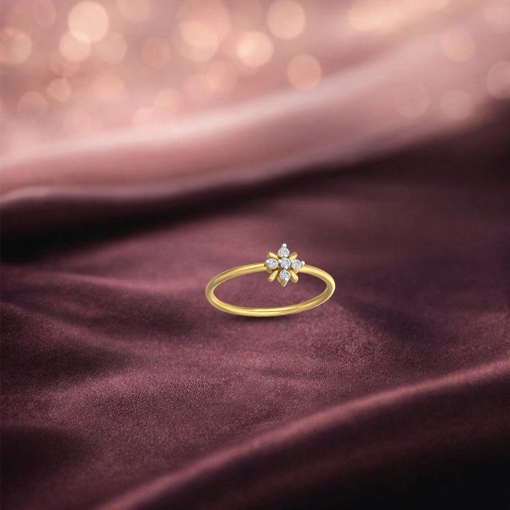 A delicate gold ring featuring a small flower-shaped, resting on draped dark plum satin fabric with a soft pink bokeh background.