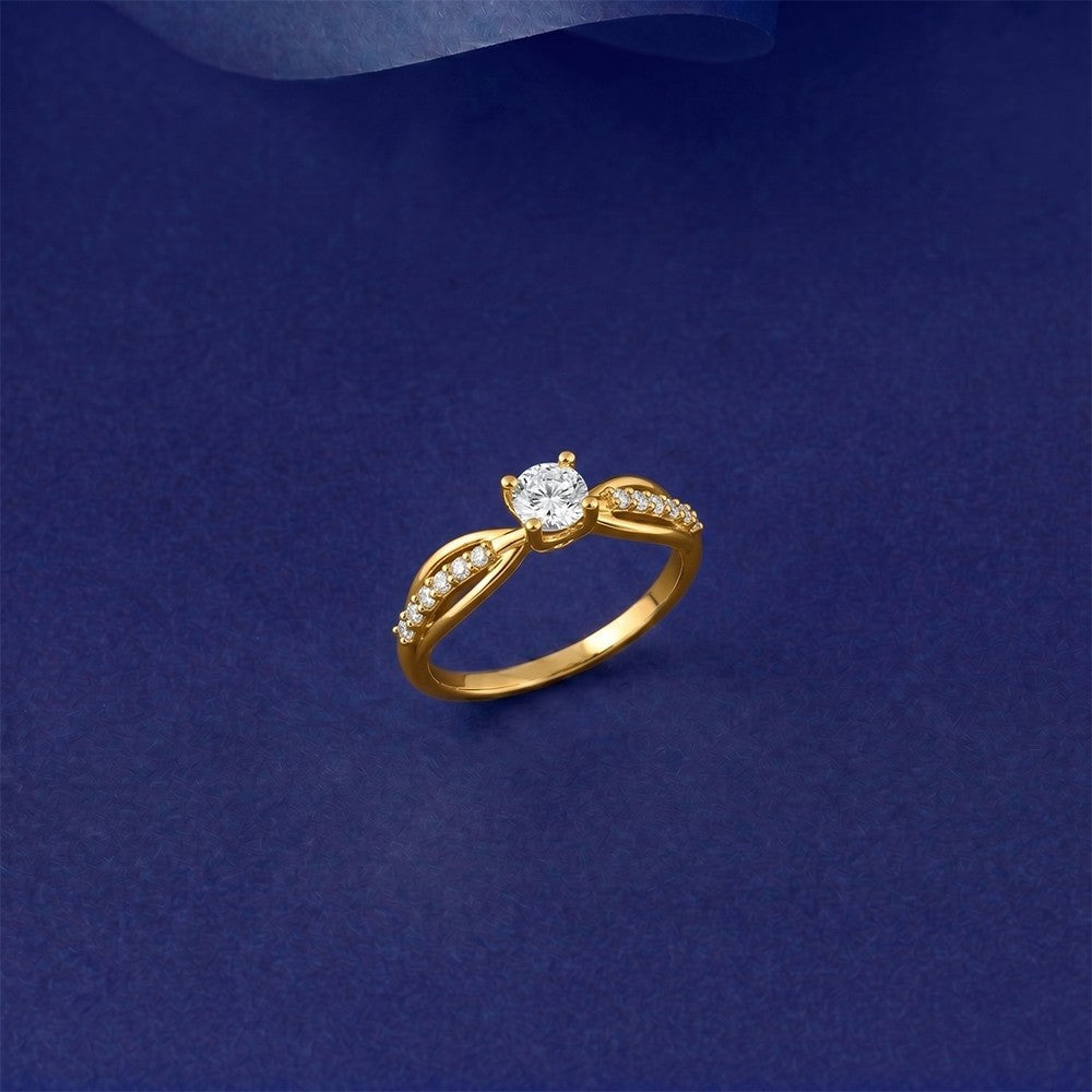 A gold ring with a round-cut center stone, displayed on a dark blue textured background.
