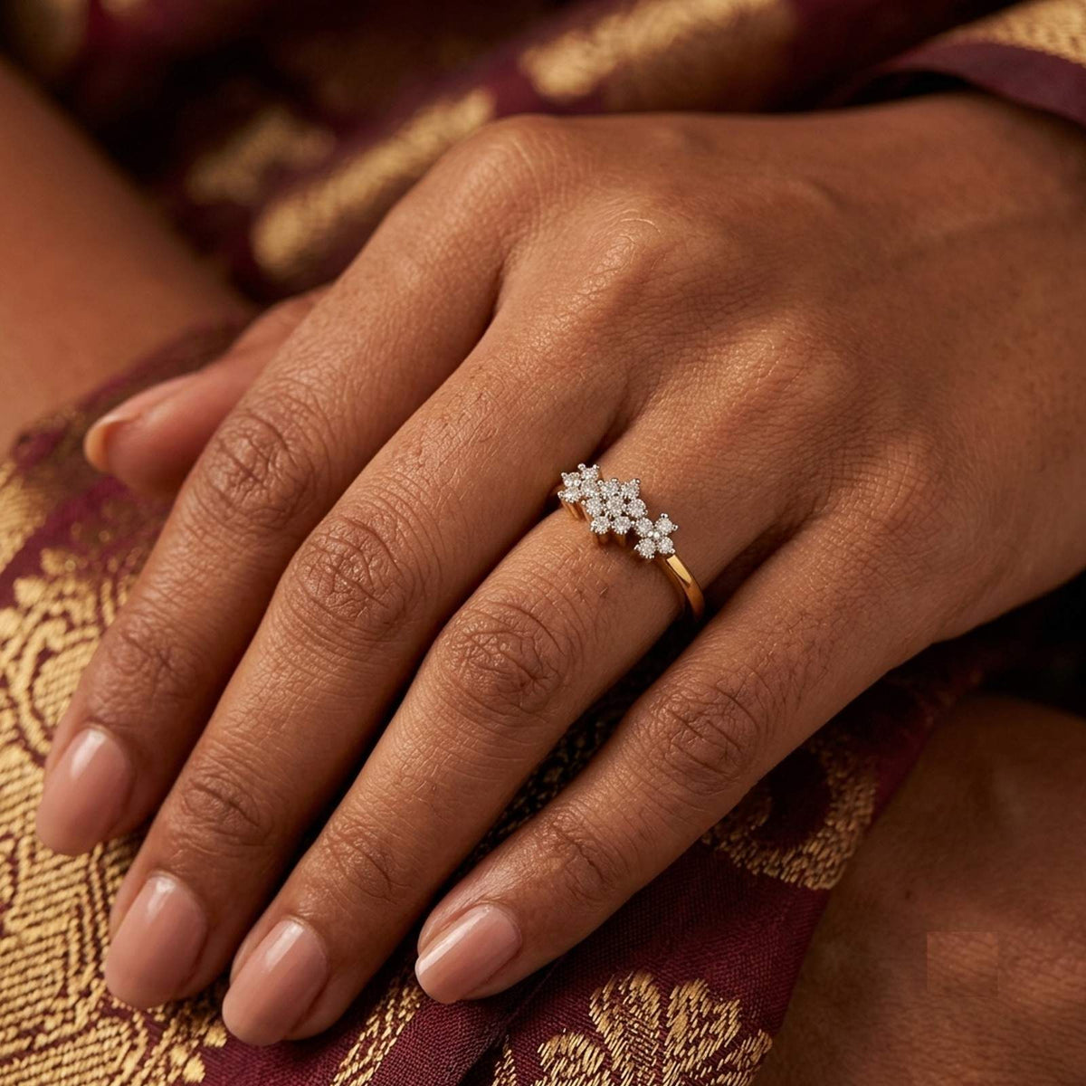 A close-up of a hand wearing a delicate gold ring adorned with a floral cluster setting.