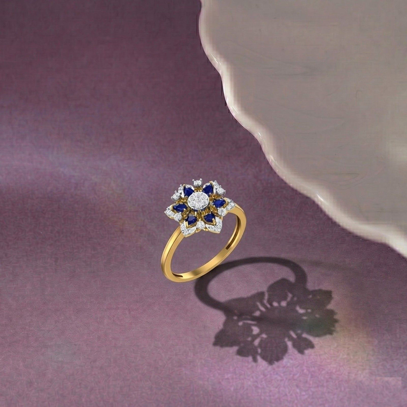 A gold ring with a floral cluster setting featuring a central round, displayed on a purple surface.