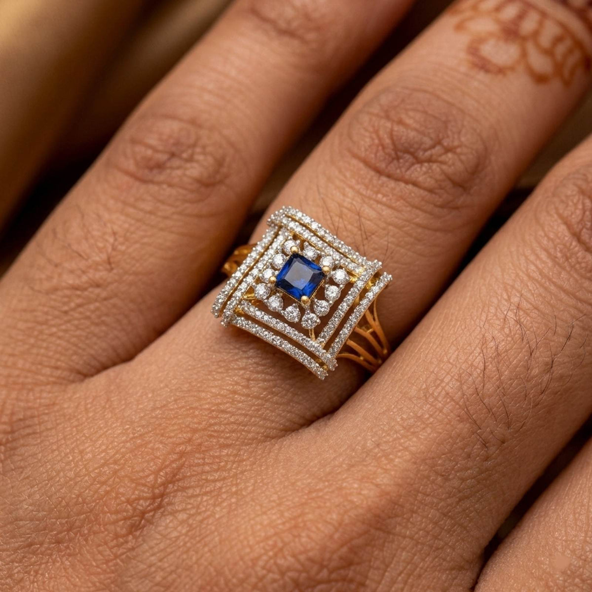 A close-up of a hand wearing a square ring with a blue center stone, resting over a dark brown woven surface.