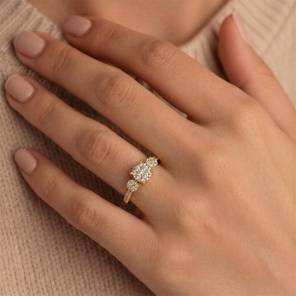 A close-up of a hand wearing a gold ring diamond center, set against a soft beige knit sweater.