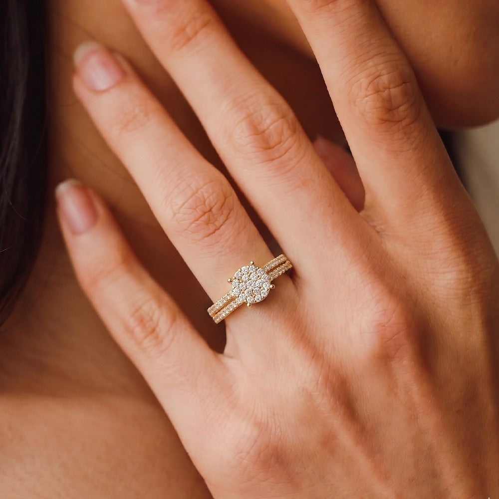 A close-up of a woman's hand wearing a gold ring with a round-cut diamond cente.