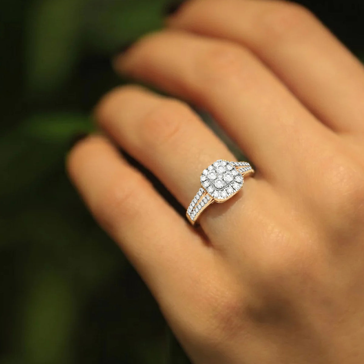 Rose gold ring with diamonds on a hand against a blurred green background