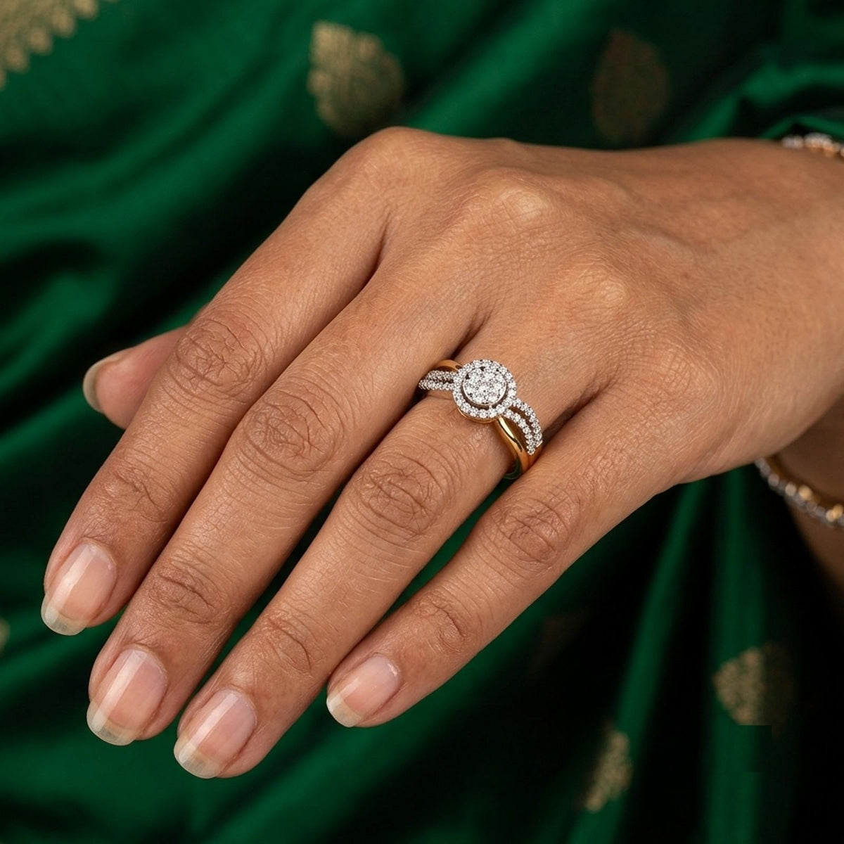 A close-up of a hand wearing a round diamond center and a surrounding halo, set against a dark green satin fabric background.