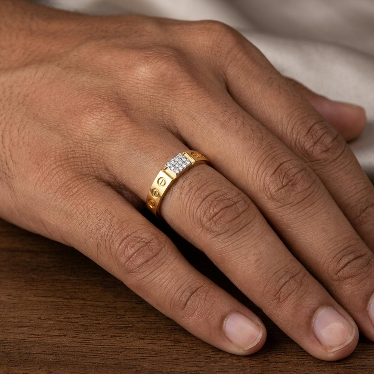 A gold ring with a row of small clear stones on the ring finger of a hand, resting on a wooden surface.
