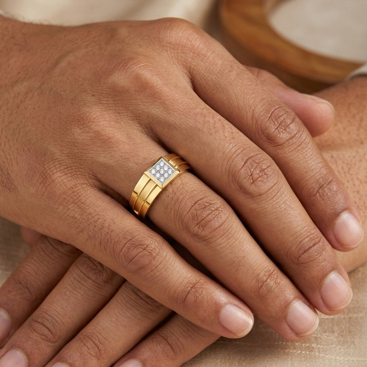 A close-up of a gold ring with a square diamond cluster setting worn on a finge.
