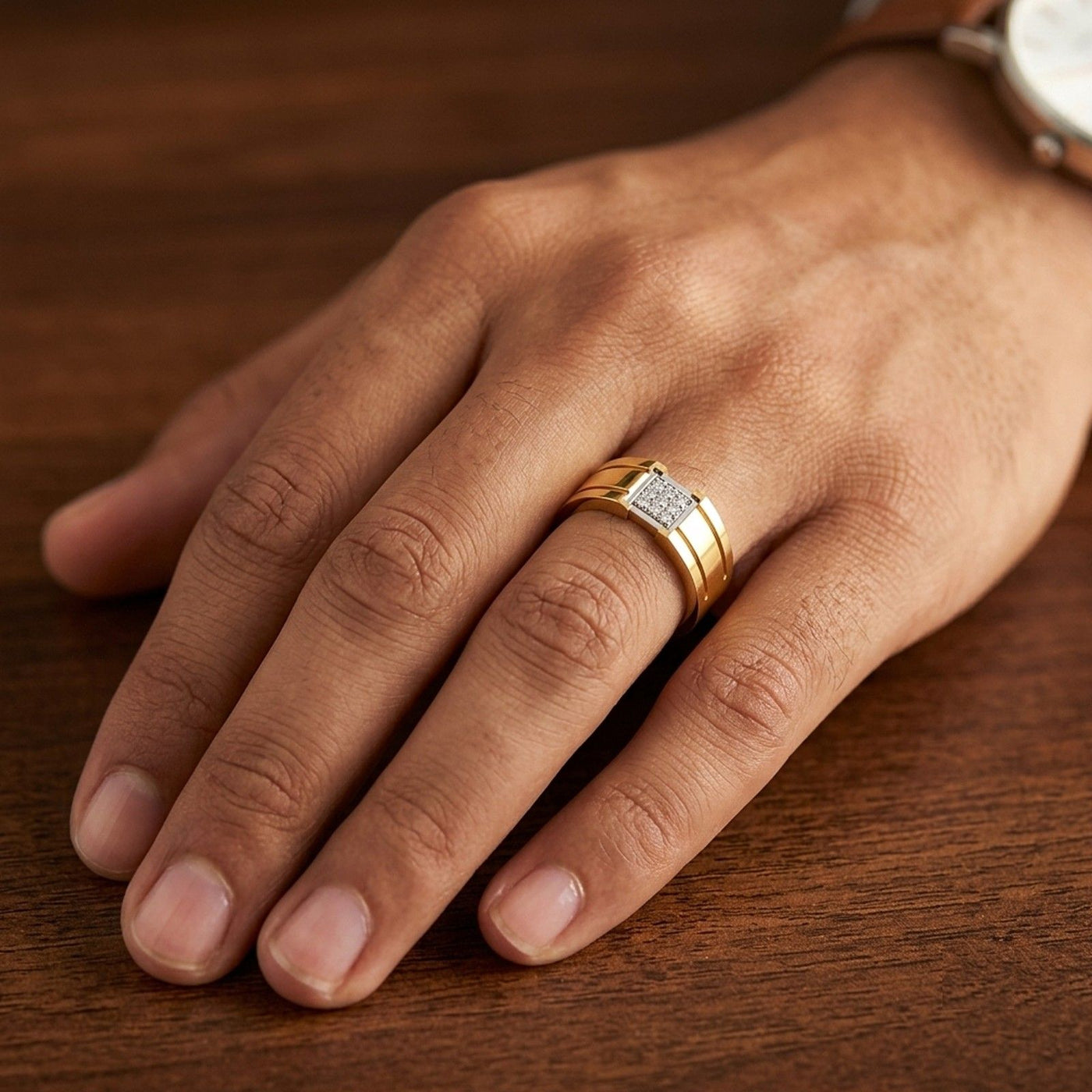 A close-up of a hand resting on a dark wooden surface, wearing a yellow gold ring with a square design.