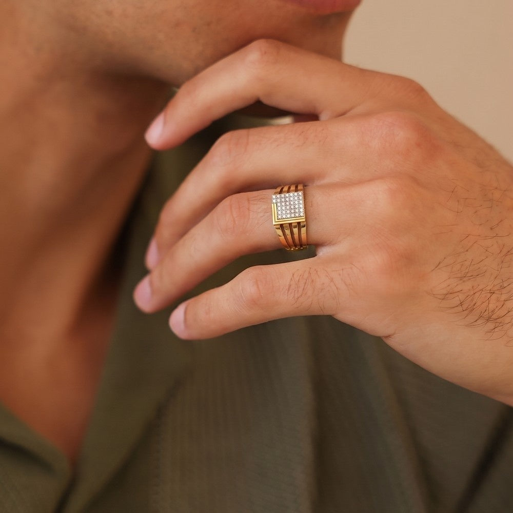 Close-up of a hand wearing a gold ring with a diamond pattern, against a neutral background.
