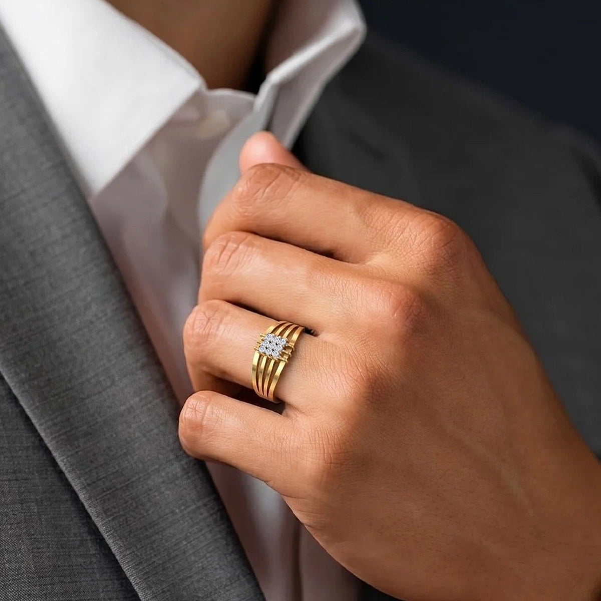 A close-up of a person's hand wearing a gold ring, styled with a white dress shirt and gray suit jacket.