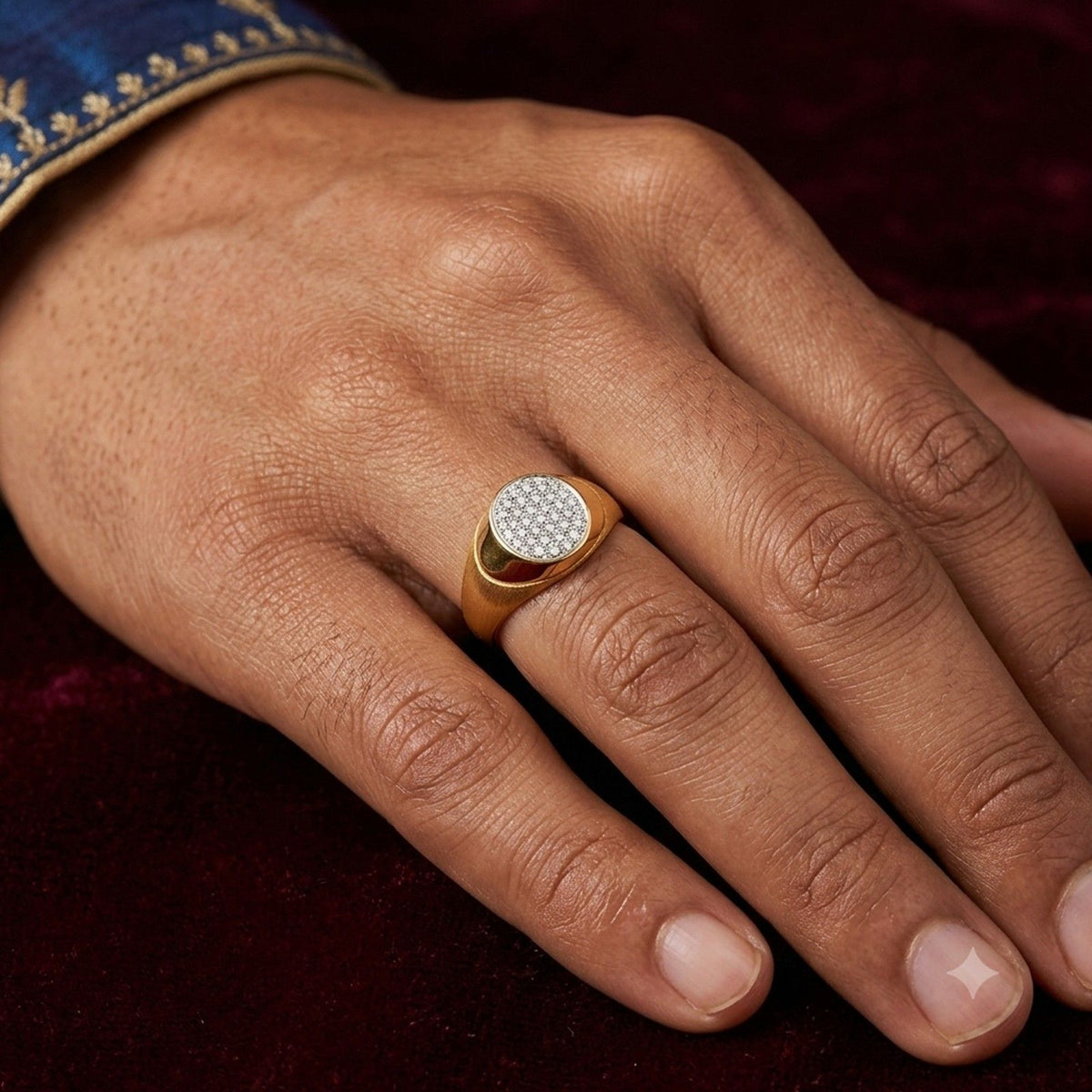 A close-up of a man's hand wearing a gold signet ring with a round, diamond-paved face.