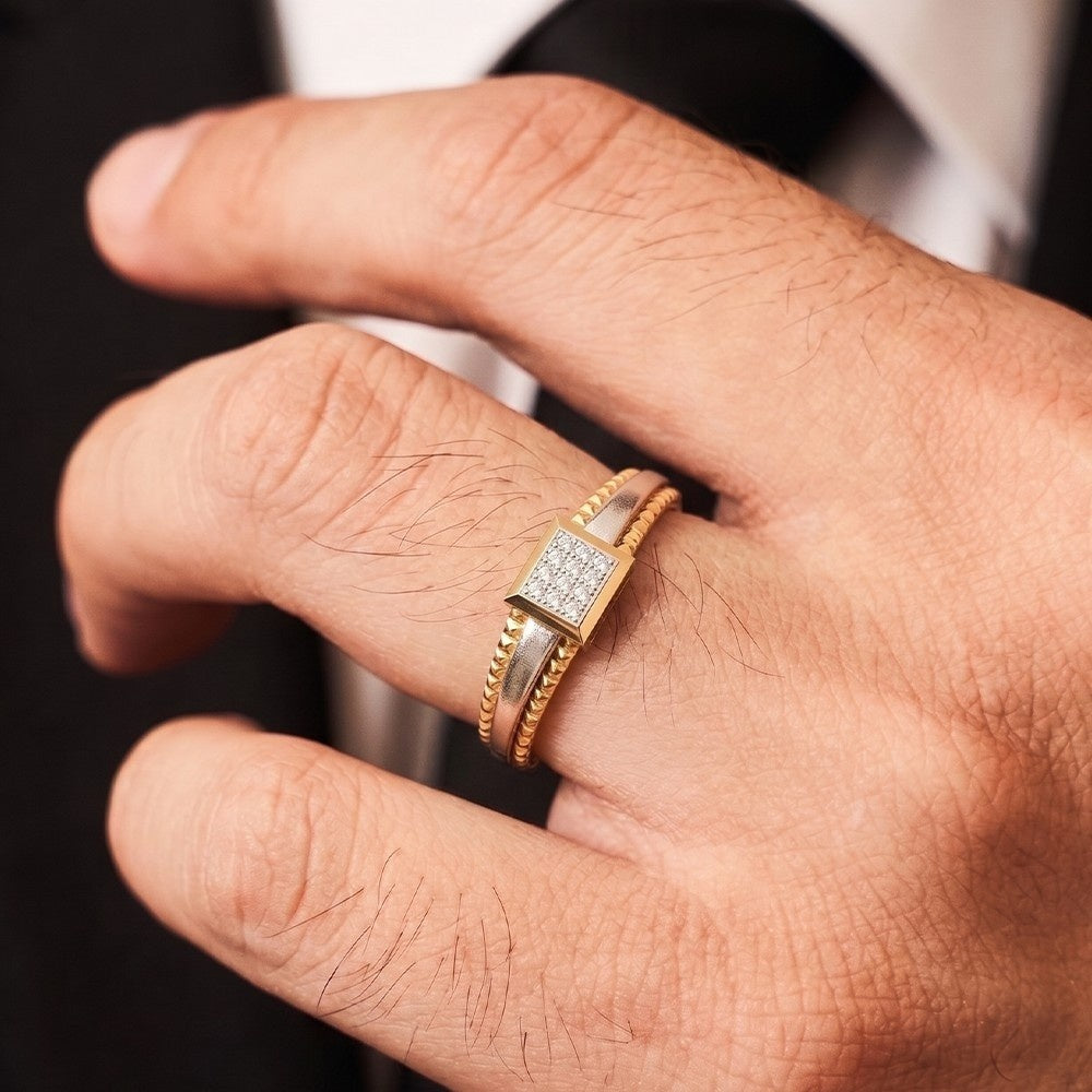A close-up of a man's hand wearing a gold ring with a square diamond-set center and a textured band.