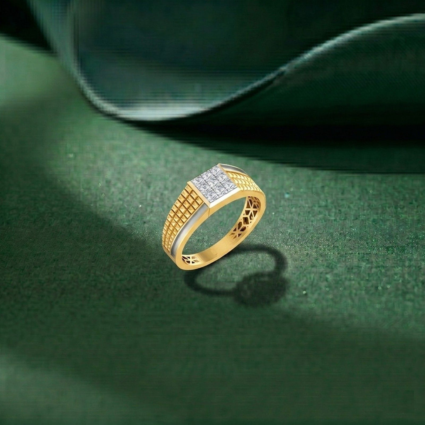 A gold and diamond ring with a square-cut setting and textured geometric bands, resting on a dark green textured surface with a soft shadow.