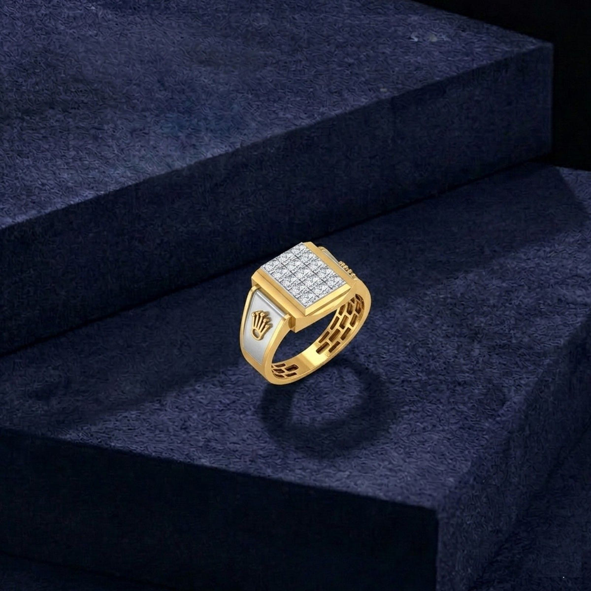 A gold signet ring with a square face paved with clear stones and a crown motif on the band, displayed on a dark textured pedestal.