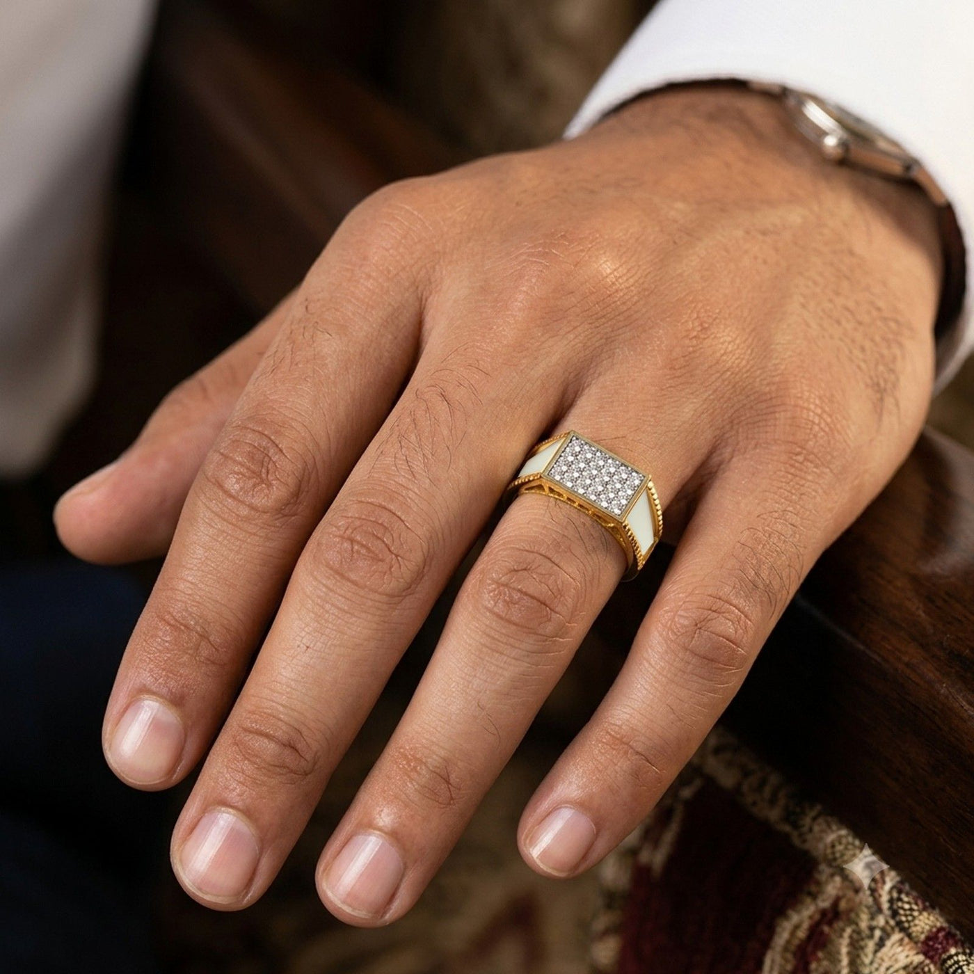 A close-up of a man's hand wearing a gold signet ring, resting on a dark wooden surface.