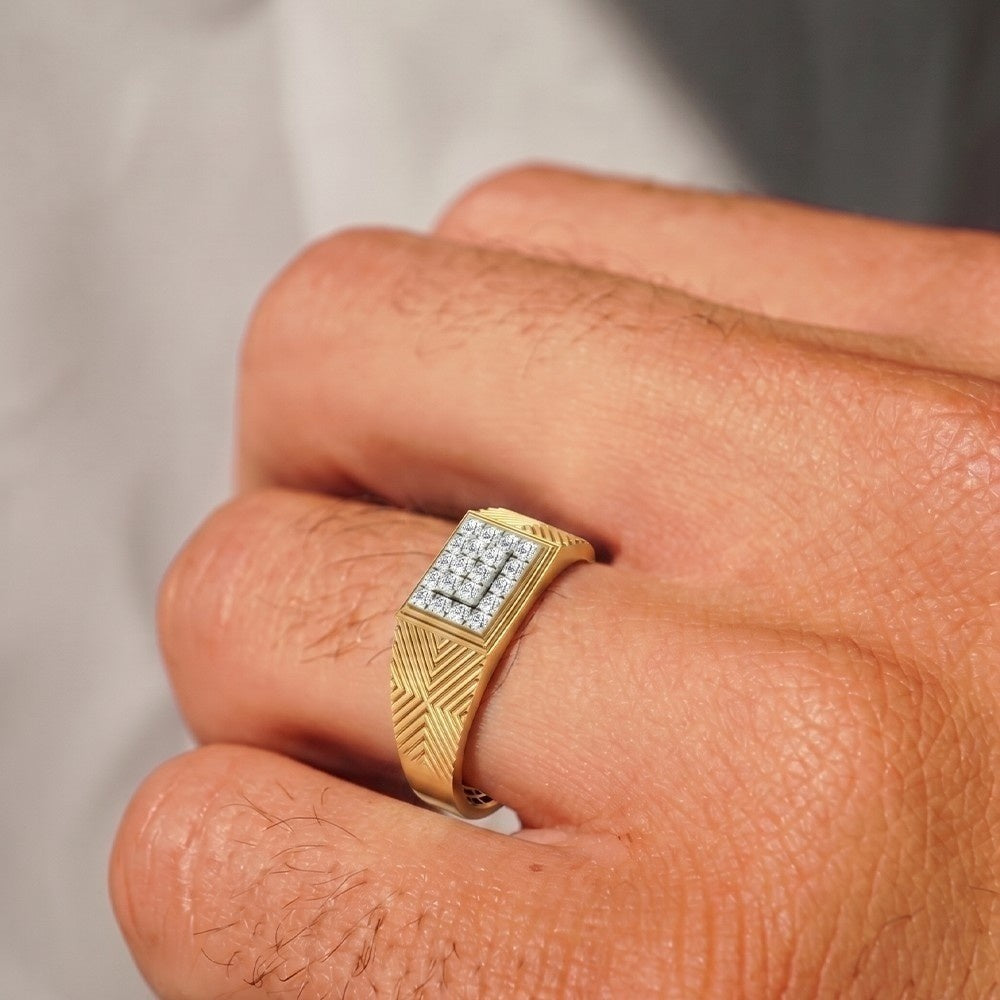 A close-up of a gold signet ring with a square diamond pavé setting, worn on a person's finger.