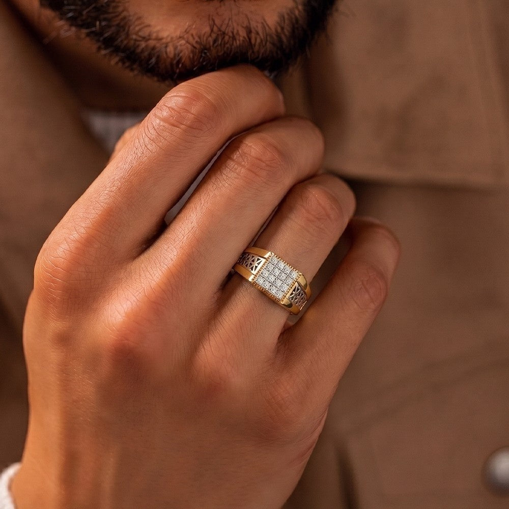 A close-up of a man's hand wearing a gold ring with a square grid of, set against a warm brown jacket background.