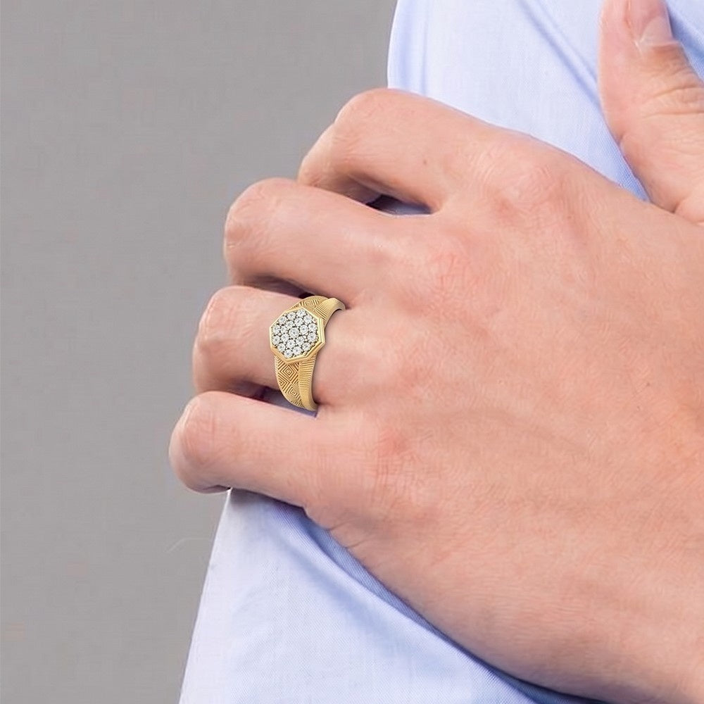 A close-up of a man's hand wearing a gold signet ring with a pavé diamond center, resting on his light blue shirt.