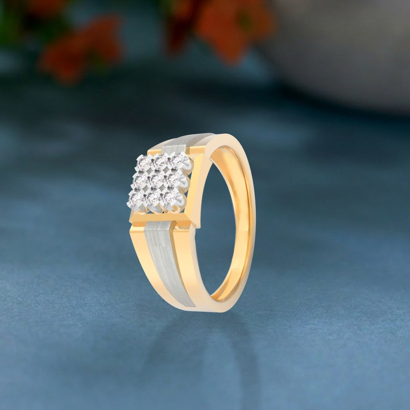 Gold and diamond ring featuring a square cluster, on a teal surface.