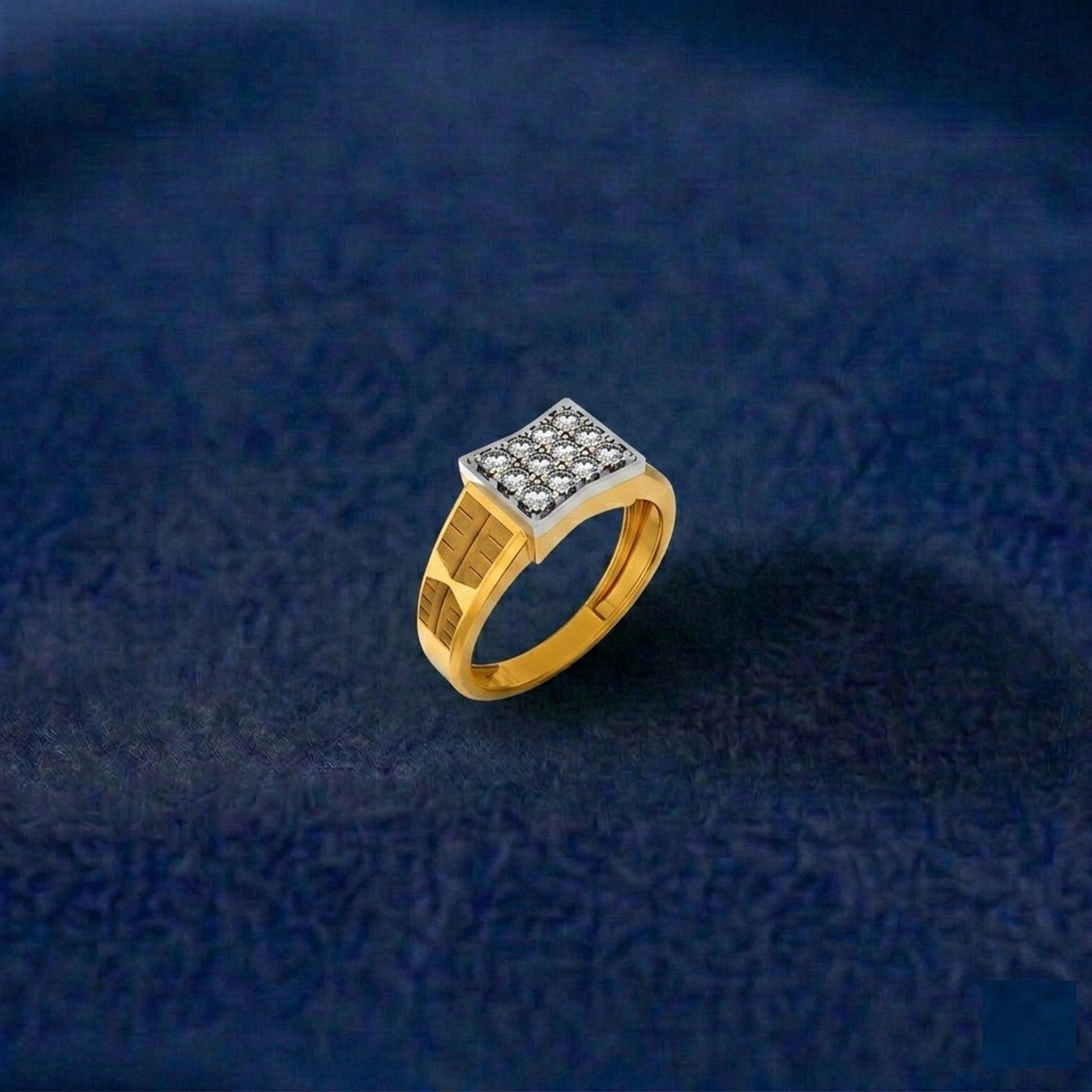 A gold ring with a square diamond-studded top, photographed on a dark navy blue textured fabric background.