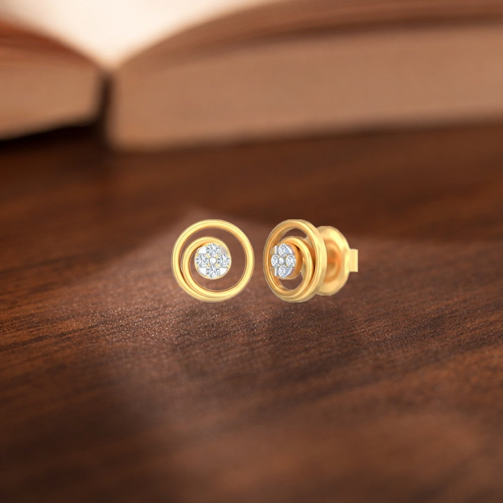 A pair of gold and diamond stud earrings with a circular design, resting on a dark wooden surface.