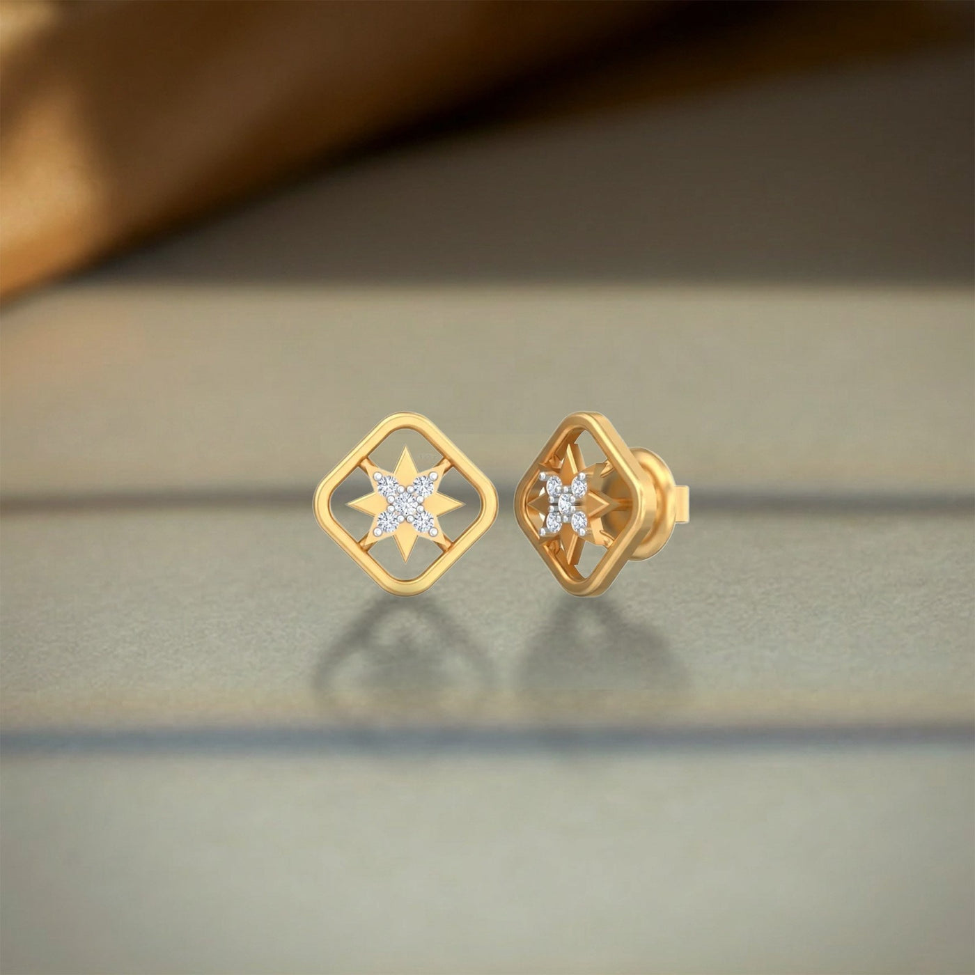 A pair of gold and diamond geometric stud earrings with starburst center details, shown on a neutral gray reflective surface.