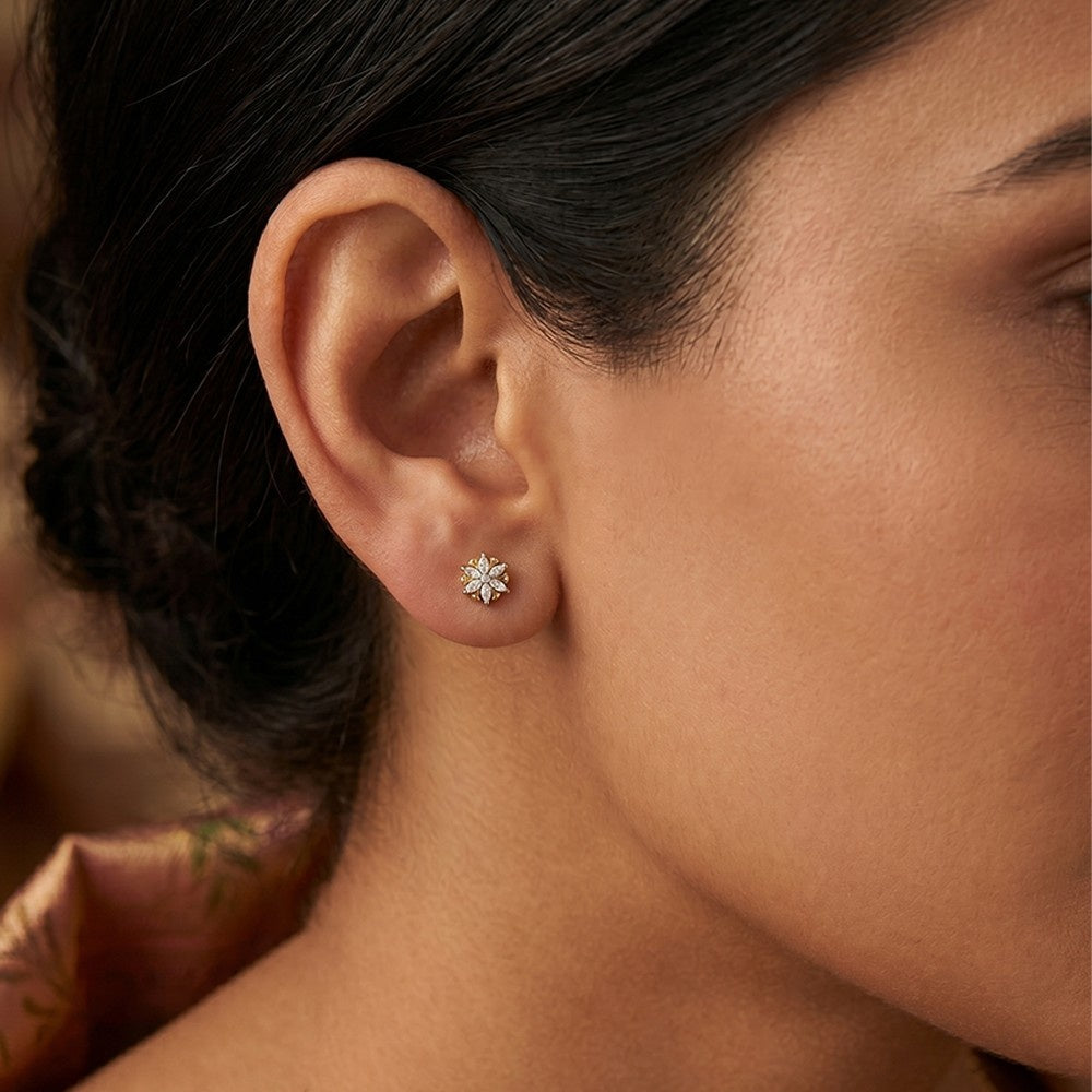 A close-up of a model's ear wearing a gold and diamond floral-shaped stud earrings.