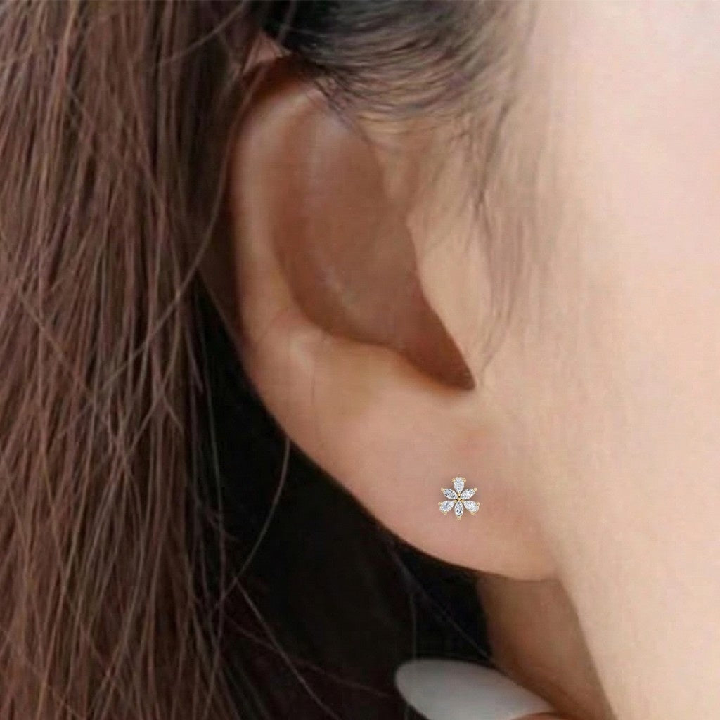 A close-up of a person's ear wearing a gold and diamond flower-shaped earrings.