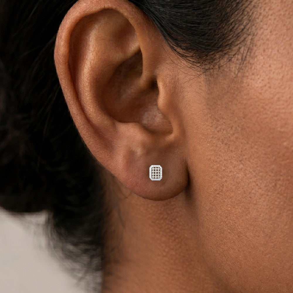 A close-up of a person's ear wearing a small rectangular stud earring.