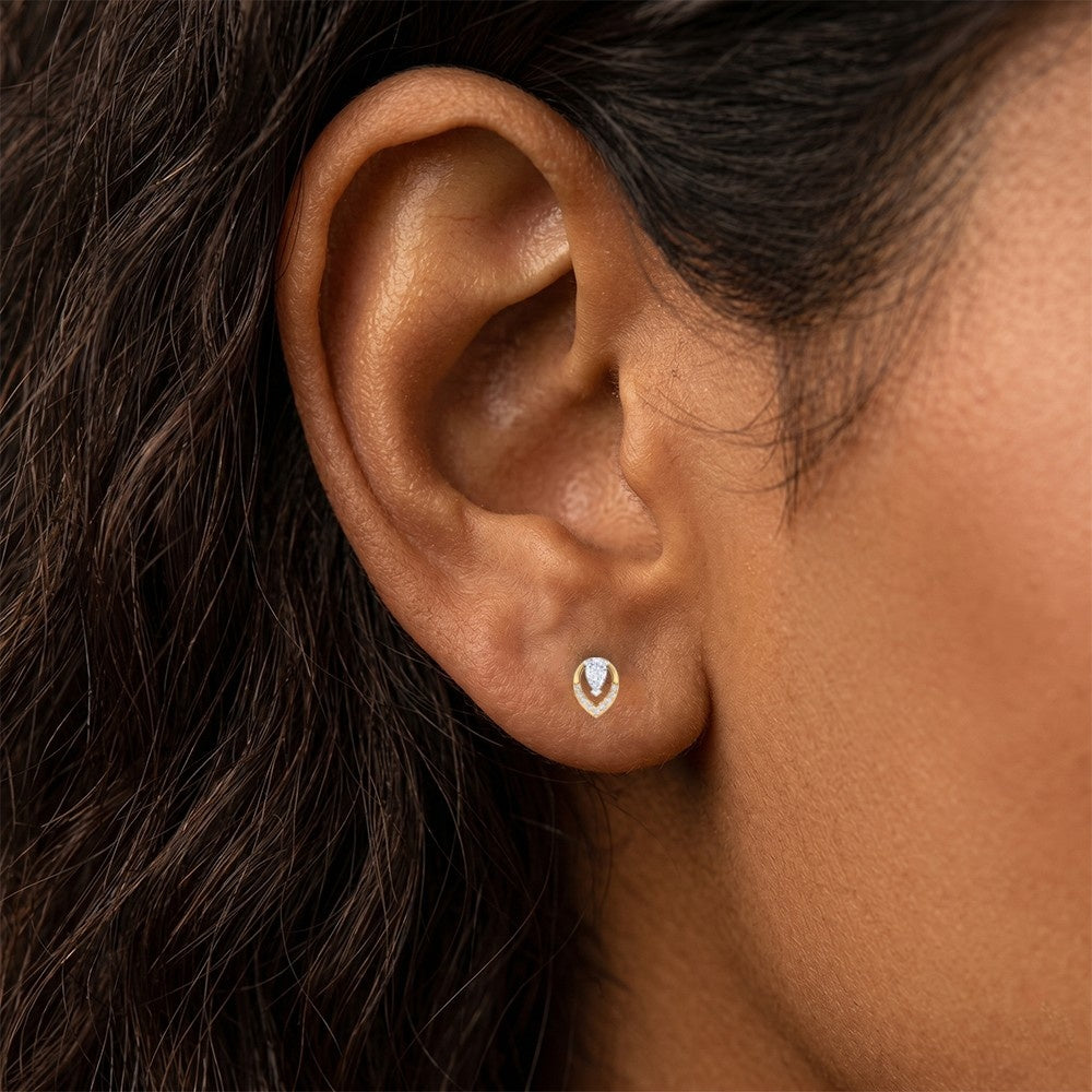 A close-up of a model's ear wearing a gold and diamond earrings on a white background.