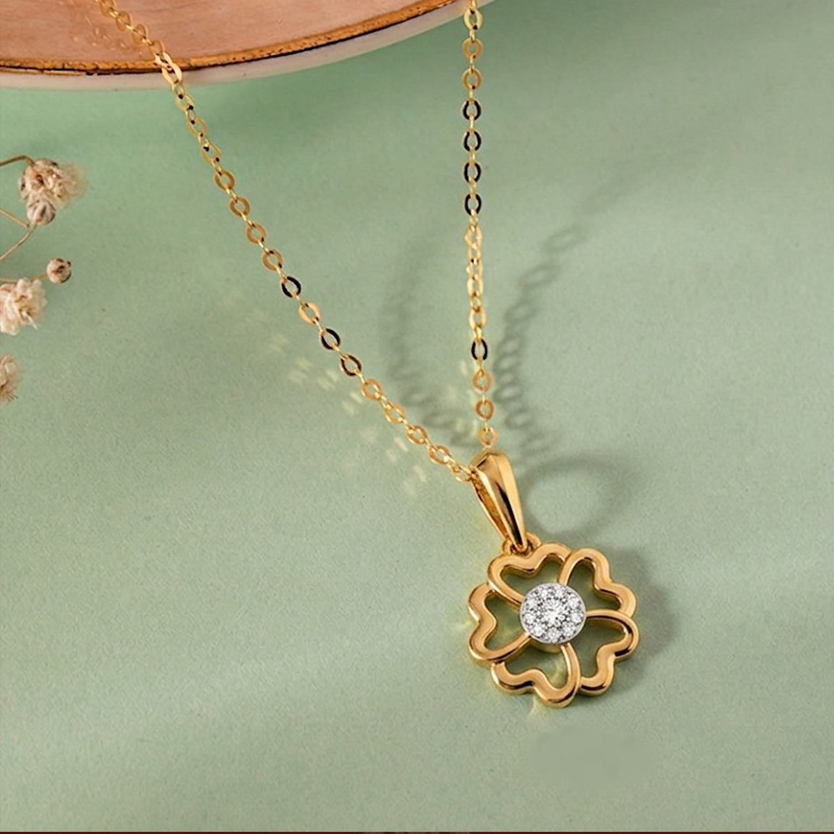 Gold with a floral pendant on a reflective surface with a green background