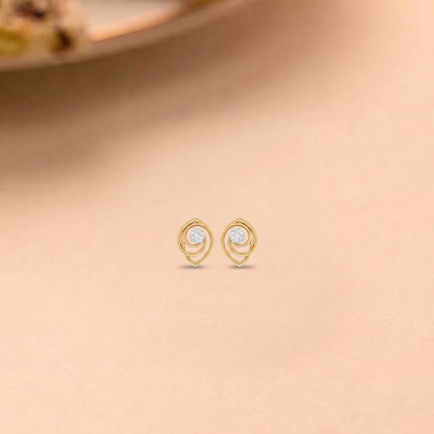 Gold and diamond stud earrings with circular design  on a beige background.