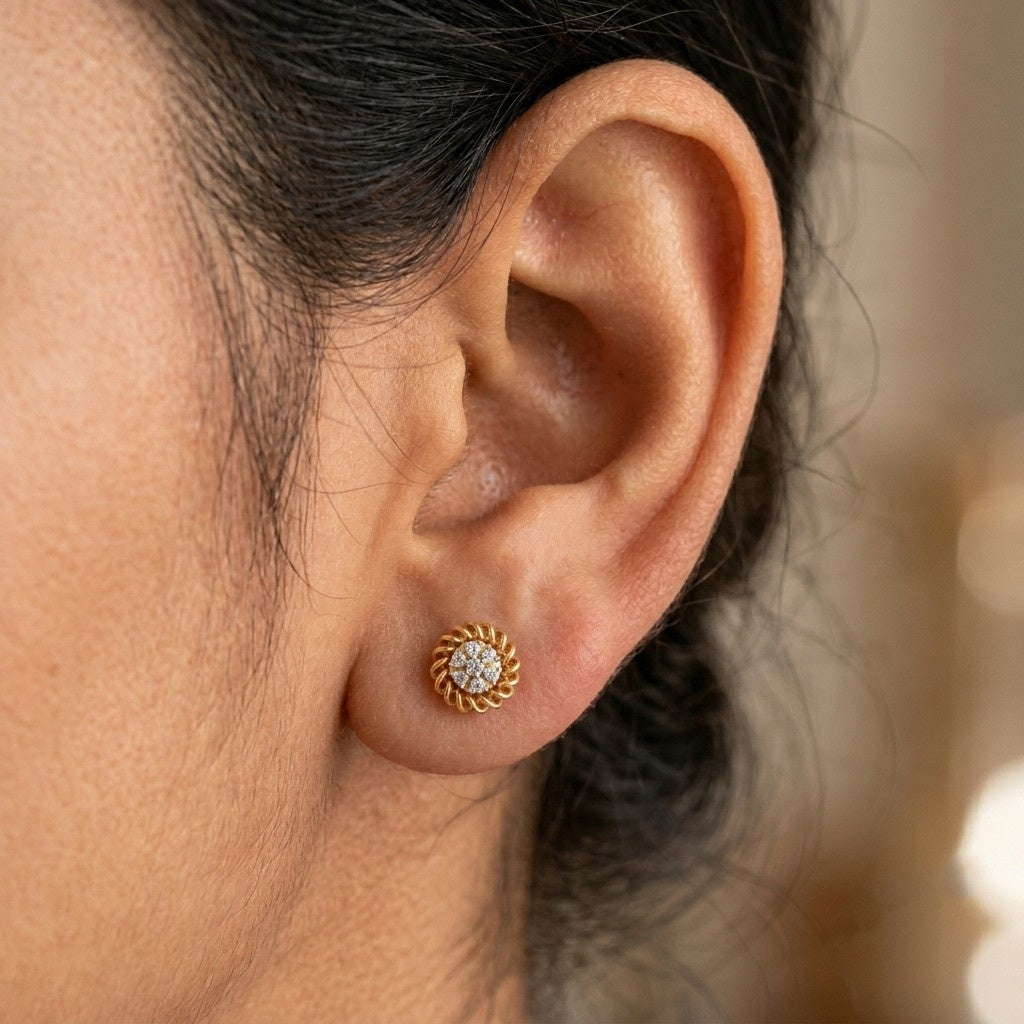 A close-up of a person's ear wearing a gold stud earring with a circular design.