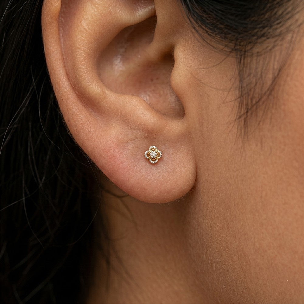 A close-up of a person's ear wearing a small gold stud earring with a central diamond detail.