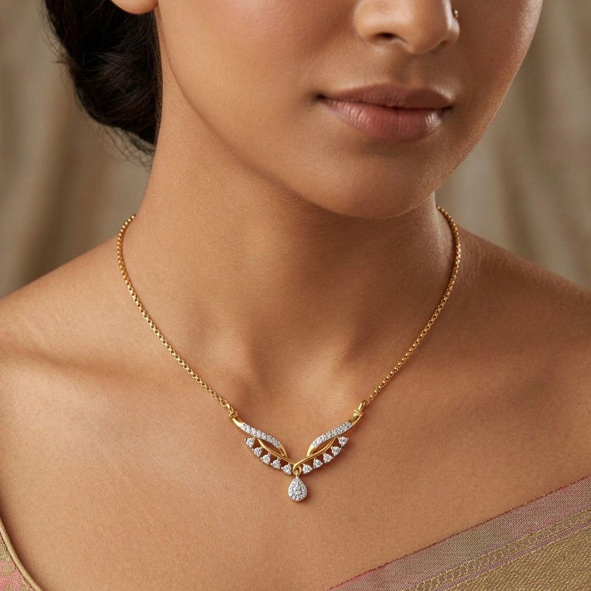 A close-up of a woman wearing a delicate gold mangalsutra with small clear stones and a teardrop drop, shown against her neck and upper chest.