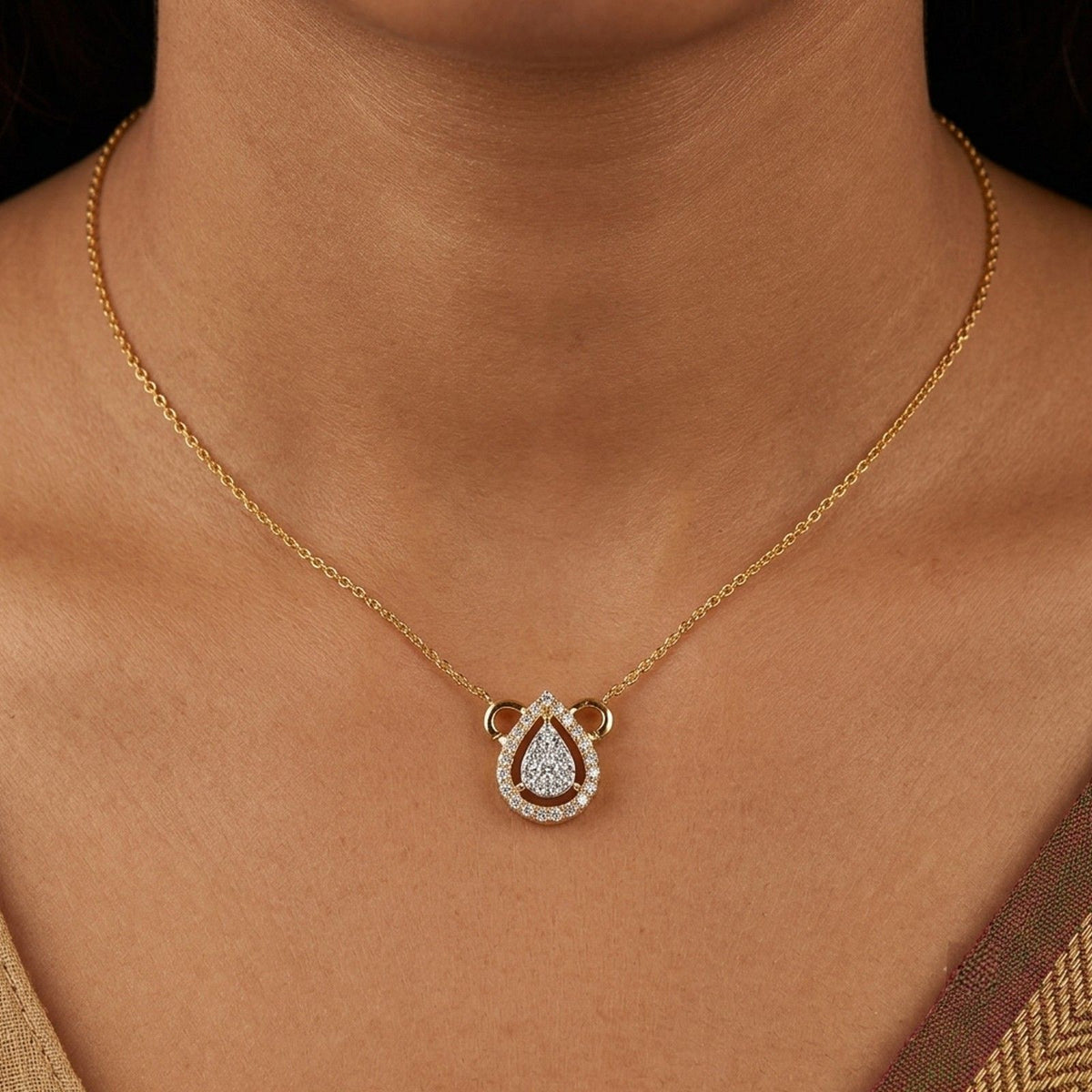 A close-up of a gold chain mangalsutra with a teardrop-shaped with clear stones, worn on a model's neck.