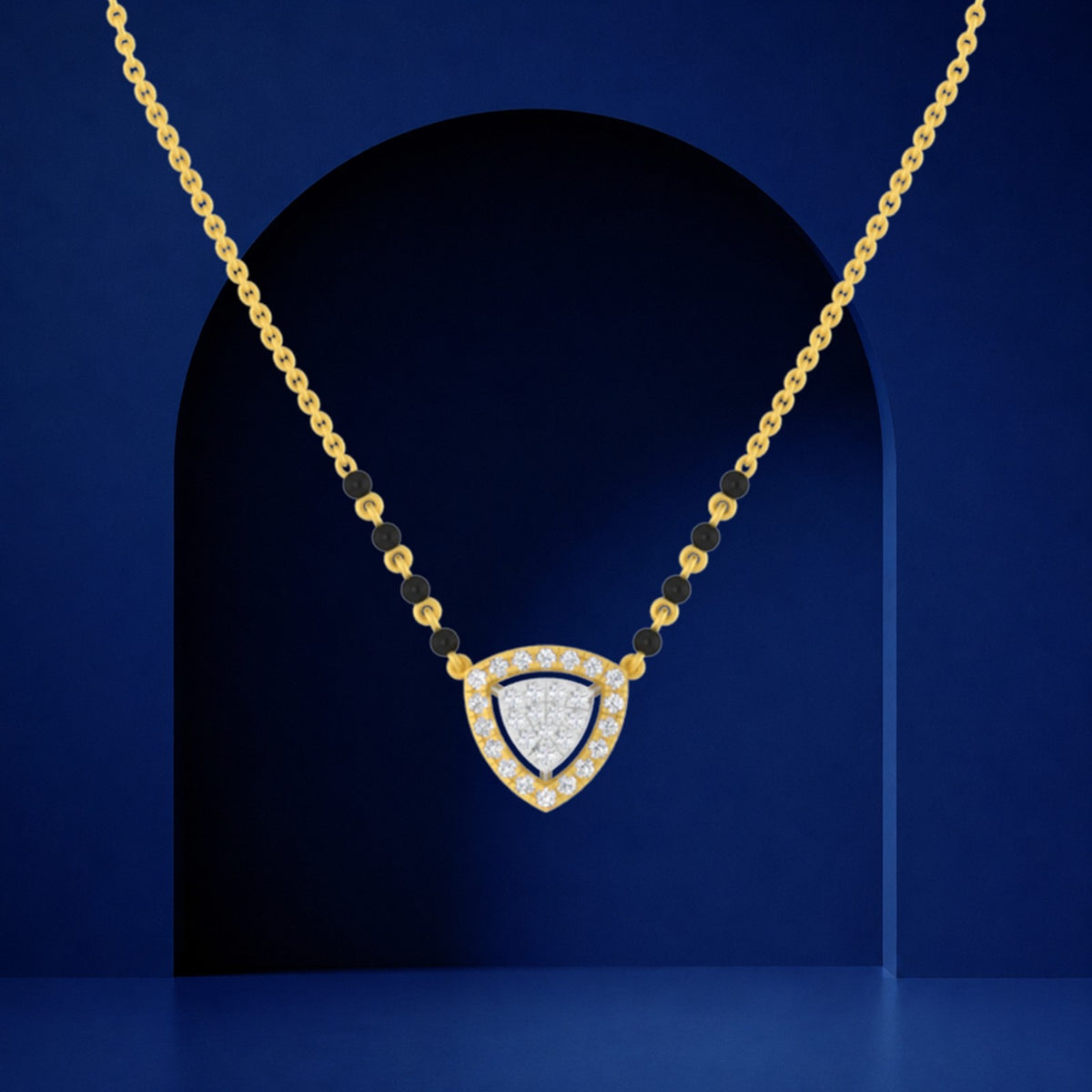 Delicate mangalsutra featuring a gold link chain with small black beads and a triangular pendant with a diamond-encrusted center and gold frame, displayed against a royal blue arched background