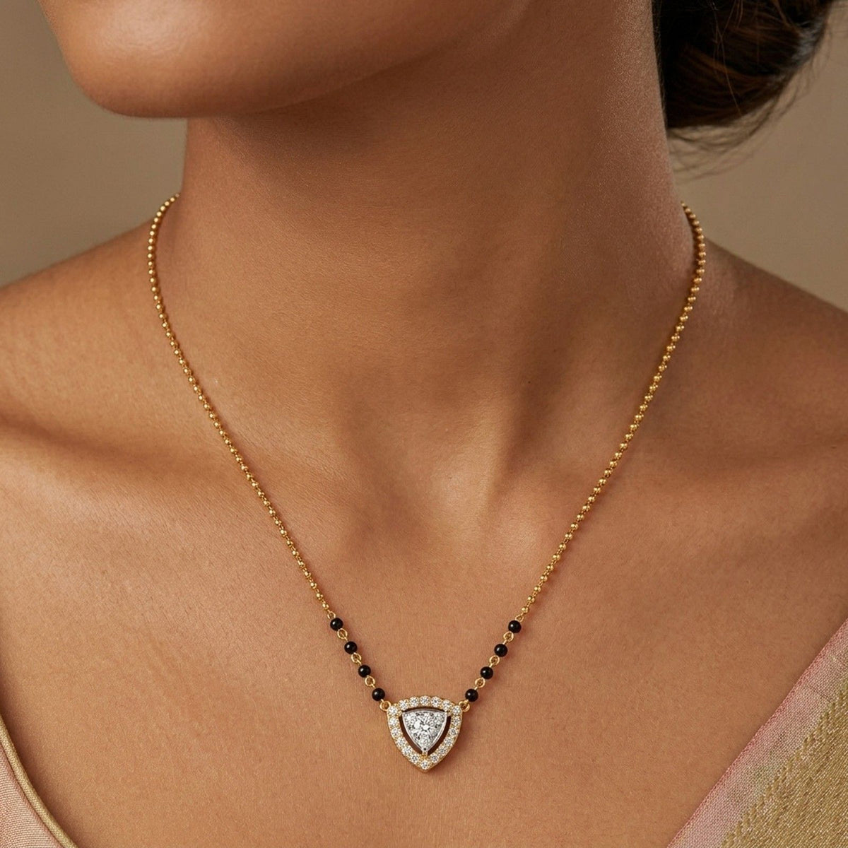 A close-up of a person wearing a gold beaded mangalsutra with small black beads and a layered, triangular diamond